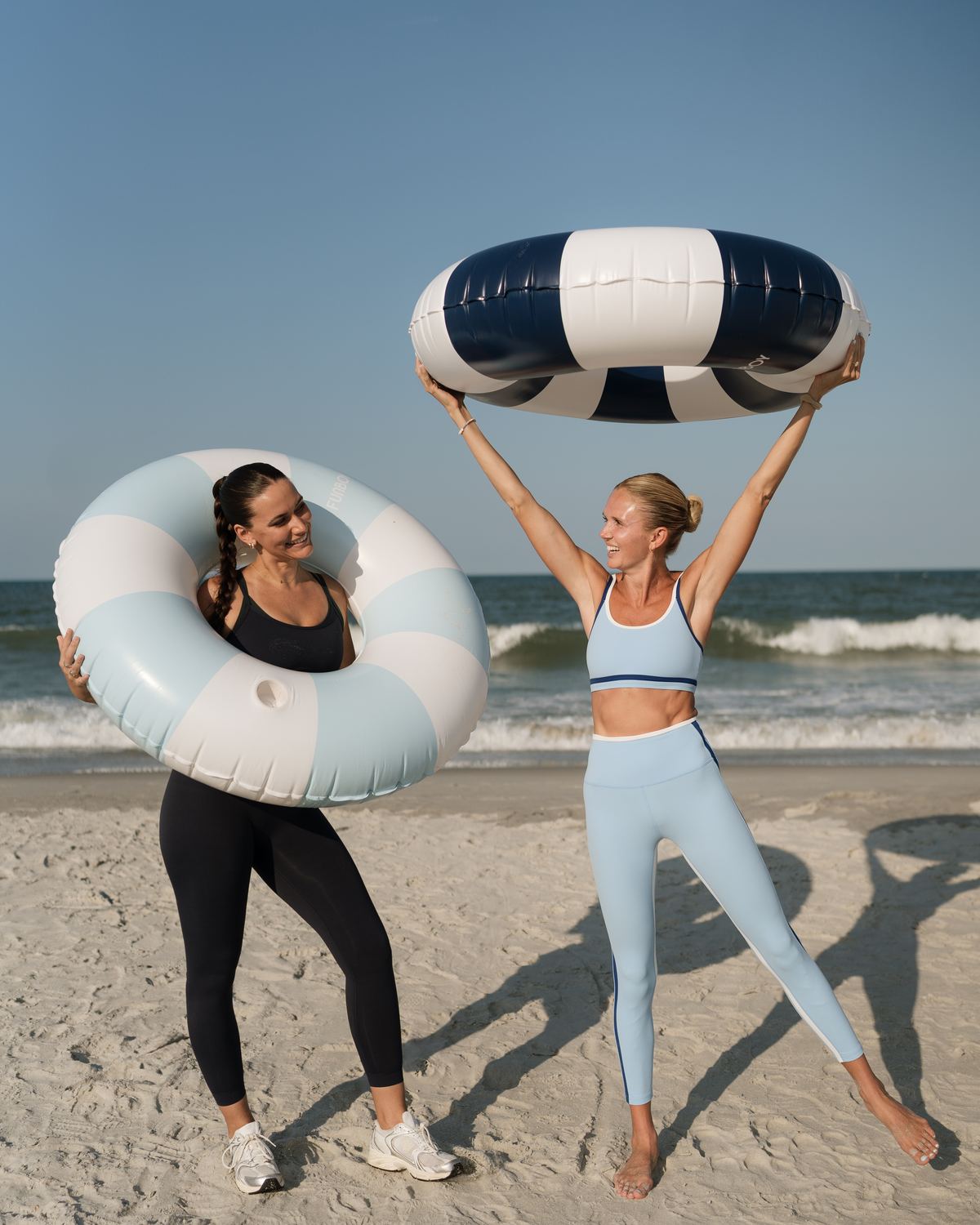 Two members playing with striped pool floats on the beach